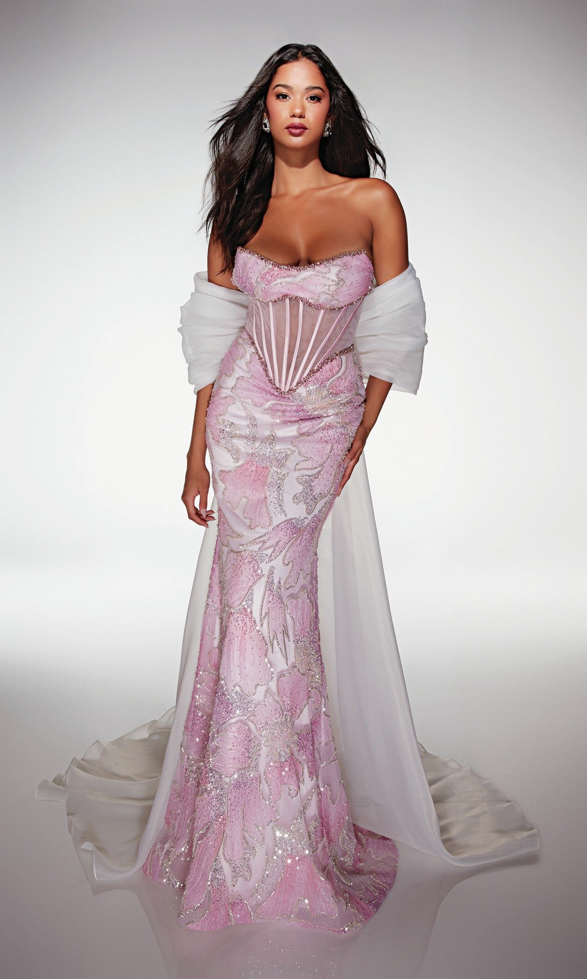 A woman wears the Alyce 62187 Long Prom Dress—a strapless, form-fitting pink and white floral gown with a sheer corset bodice, floral embellishments, and a trailing sheer white shawl.